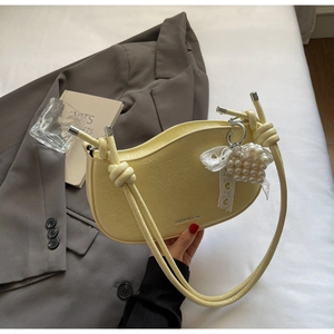 Detail of light yellow matte shoulder bag with knotted strap and pearl bow charm