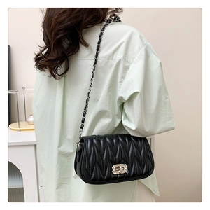 Rear view of a black vertical quilted chain bag with rhinestone lock worn on a shoulder