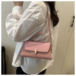 Pink crossbody bag with gold buckle shown on shoulder of a model in white shirt