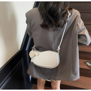 Detail view of a white crescent shoulder bag with a pearl heart charm on a grey blazer