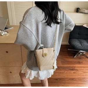Detail of beige woven bucket bag featuring a gold twist lock and metal chain strap