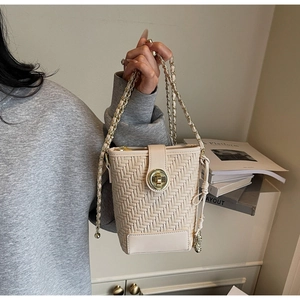Detail of woven bucket bag featuring gold rotating lock and elegant chain strap