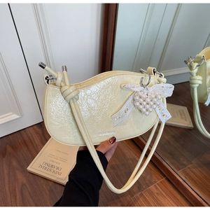 Detail of light yellow shoulder bag featuring crinkled texture and heart pearl charm