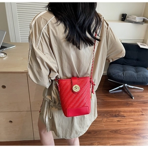 Red woven bucket bag with gold clasp and chain strap shown on a model's shoulder
