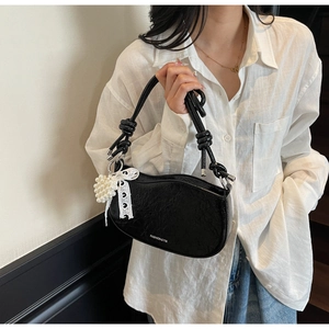 Detail of black pleated patent leather underarm bag with pearl and lace bow charms
