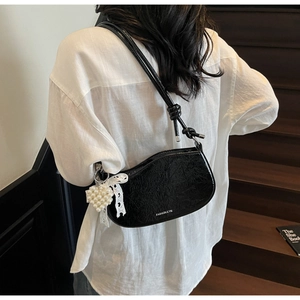 Detail view of black glossy shoulder bag with lace bow and pearl heart charm on a model