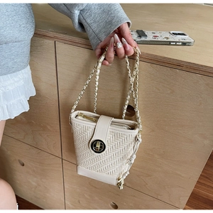 Detailed view of beige woven bucket bag with gold clasp and chain strap held by hand