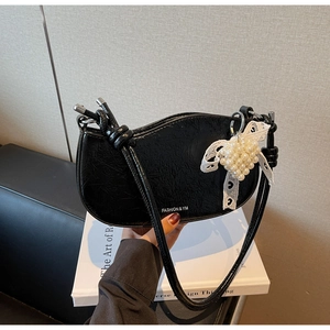 Detail of black crescent shoulder bag featuring lace bow and pearl heart pendant charm