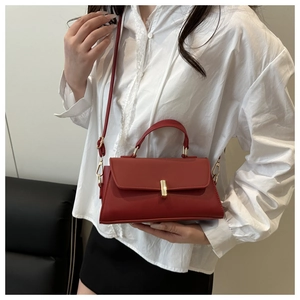 Detailed close-up of a red structured leather handbag with a gold twist lock and shoulder strap