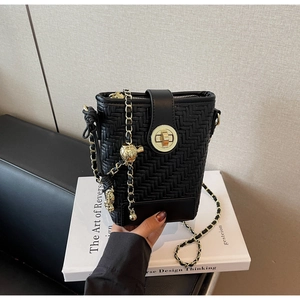 Detail of black woven bucket bag showing golden twist lock and chain strap with charms
