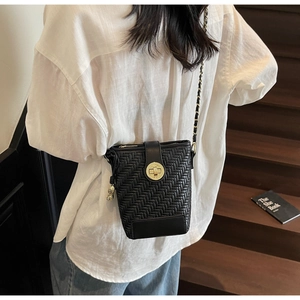 Detail of black woven bucket bag showing golden twist lock and chain strap on stairs