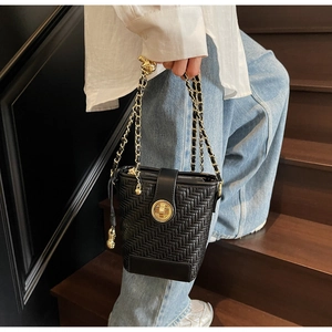Detail of black woven bucket bag with gold clasp and chain strap on wooden stairs