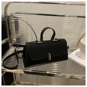 Detail of minimalist black handbag featuring a sleek golden cylinder metal clasp