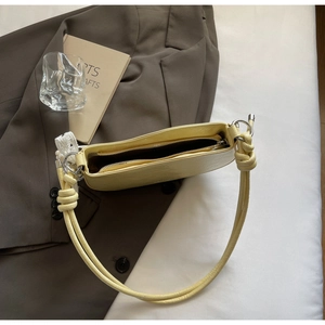 Detail of light yellow underarm bag with knot strap and white lace bow accessory