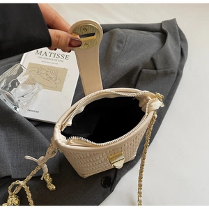Macro shot of beige woven bucket bag showing gold hardware and peanut charm detail