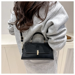 Detail of black trapezoid crossbody bag featuring gold metal cylindrical lock and handle