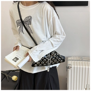 Detail of black rivet bucket bag with silver eyelets and pearl chain on a stylish model