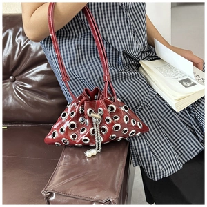 Close-up of burgundy bucket bag with silver eyelets and pearl chain on a dress