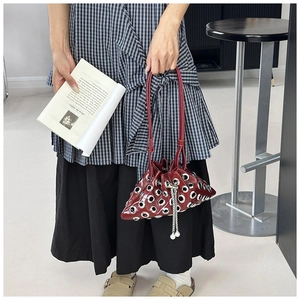 Detail of burgundy bucket bag with silver eyelets, drawstring chain and pearl charms