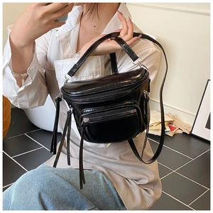 Détail d'un sac à bandoulière noir avec poches zippées multiples et longs pompons