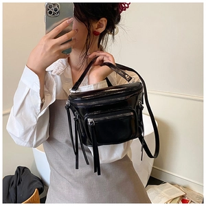 Détail du sac seau en cuir verni noir avec fermetures éclair et longs glands décoratifs