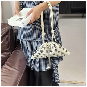 Detail of off-white rivet bucket bag with silver eyelets and pearl chain on a blue dress