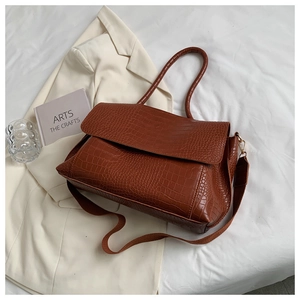 Detail of dark brown crocodile texture handbag on a white bed sheet with aesthetic props