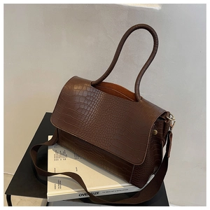 Detail of dark brown crocodile embossed tote bag with wide textile strap on art books