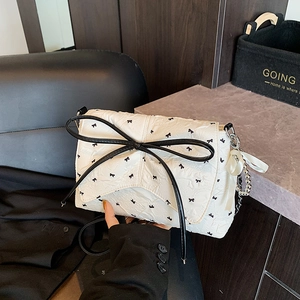 Elegante bolso de hombro beige con lazos negros y cadena decorativa con cinta blanca