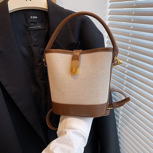 Canvas and leather bucket bag with metal lock shown in a stylish hand-held pose