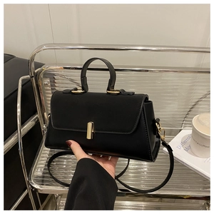 Minimalist black leather handbag with a gold cylindrical clasp and a detachable shoulder strap