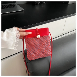 Detail of red and blue woven mini bag featuring a large pearl clasp and thin strap