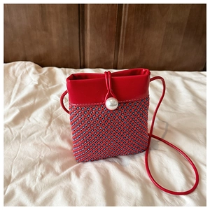 Detailed close-up of woven mini crossbody bag featuring a large pearl clasp and red leather