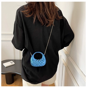 Glossy blue acrylic shell bag with quilted texture and gold chain strap in use