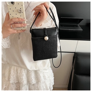 Detailed view of mini straw crossbody bag featuring large pearl clasp and black woven texture
