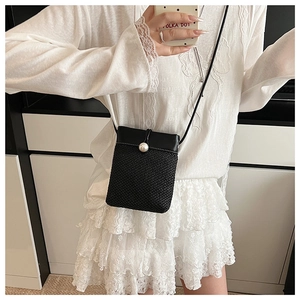 Close-up of black woven mini crossbody bag with a large white pearl fastener detail