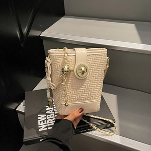 Creamy woven bucket bag with gold chain strap and turn-lock closure on grey steps