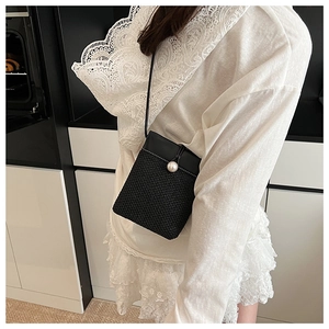 Close-up of mini black straw crossbody bag with large pearl buckle detail on model