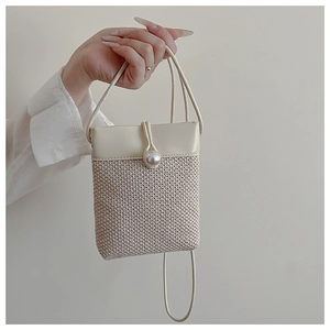Close-up of woven straw mini bag with premium leather flap and large pearl closure