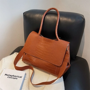 Caramel brown crocodile embossed tote bag with top handle and shoulder strap on leather chair