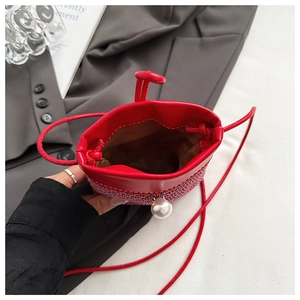 Close-up of a mini straw woven crossbody bag with pearl closure and red leather trim