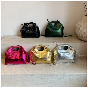 Five metallic faux leather handbags in gold, silver, and pink on a stone pedestal