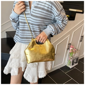 Detail of shiny gold textured faux leather bag with cut-out handle and slim shoulder strap