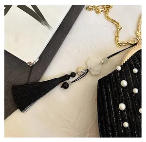 Détail du pompon en soie sur un sac perlé noir plissé avec fermoir doré métallique
