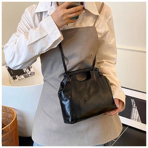 Close-up of black glossy patent leather shoulder bag with cutout handle and thin strap