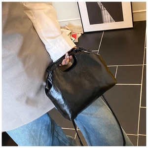 Detail of black glossy leather handbag with unique handle closure and long shoulder strap