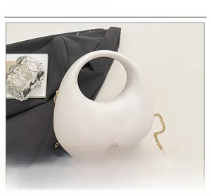 Close-up of a white crescent acrylic evening bag with a gold chain strap on a blazer