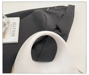 Detail of white half-moon acrylic handbag with round handle and gold chain on suit