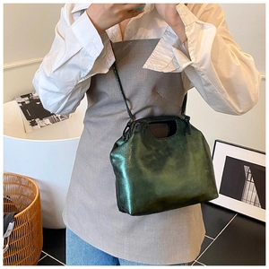 Detail of dark green metallic handbag featuring a pleated design and cutout top handle
