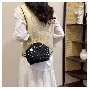 Détail d'un sac à main en perles noires avec poignée dorée et pompon fleur blanche